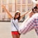 A man taking a picture in a plaza of a woman who is smiling and posing with her arms outstretched